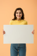 Fototapeta na wymiar Blissful smiling brunette girl holding blank placard isolated on orange