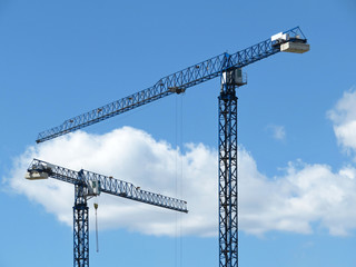 Construction cranes on background of blue sky and white clouds