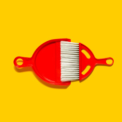 Red dustpan and brush lying on yellow background. In the style of pop art. Top view.