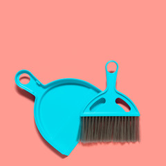 A pale blue dustpan and brush lying on living coral background. In the style of pop art. Top view. Copy space.