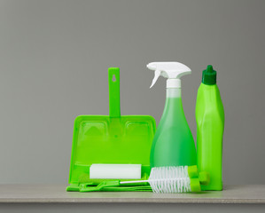 Green detergent bottle for toilet, spray bottle, brush, sponge, scoop and dust on grey background. Cleaning tools.