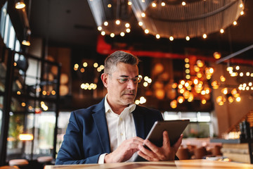 Middle aged man with serious facial expression using tablet while sitting in cafeteria.