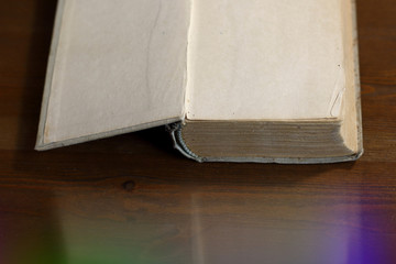 An open old retro book with white blank empty pages on which the designer can write a greeting text or a postcard on the wooden background of the library atmosphere, book light of knowledge