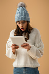 Shocked brunette young woman looking at digital tablet with open mouth isolated on beige