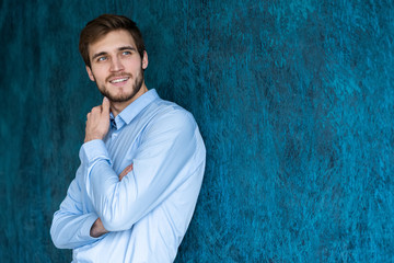 Portrait of handsome young man standing against blue wall with copy space.