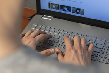 A young man typing on a laptop keyboard. Rear view, soft focus. Hard work at home