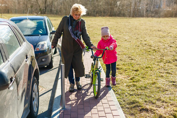 family, leisure and people concept - happy grandmother teaching granddaughter to ride bicycle at summer park