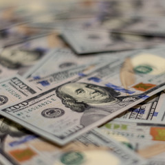 Macro shot of Benjamin Franklin's portrait on a new 100 dollar US money note, with defocused background of many more identical money notes in a mess.