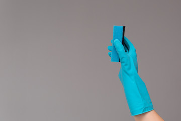 Hand in rubber glove holds color wash sponge on neutral background. The concept of bright spring, spring cleaning.