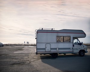 Group of young people taking pictures having fun in beach with camping caravanning motorvan mobile home parked in a coastal italian village (Imperia, Liguraia). Mediterranean europe road trip tourism.