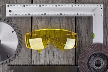 Tools for carpentry work, measurement of parts and eye protection on a wooden background.