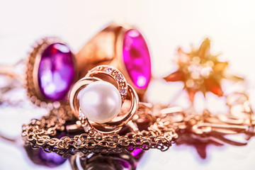 Elegant luxury composition of gold jewelry with pearl ring, amethysts and rubys gemstones on light background close-up macro and reflection