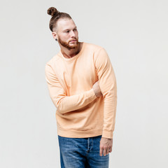 Fashionable man with beard and bun hairstyle dressed in yellow long sleeve sweater and jeans poses in the studio on the white background