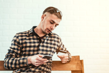 a young guy with a phone and a credit card on a bench in the room