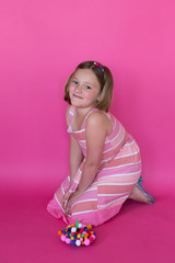Obraz na płótnie Canvas Cute smiling young girl in pink orange and white dress kneeling next to pom pom cake