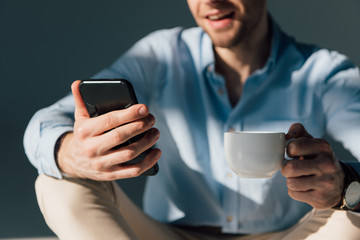 selective focus of man using smartphone and holding coffee cup