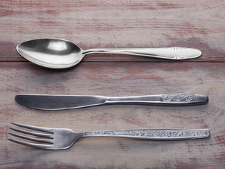 Stainless steel fork, spoon and knife on a brown wooden background with copyspace
