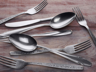 Still life of stainless steel forks, spoons and knives on a brown wooden background with copyspace
