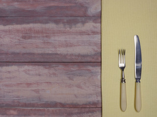 Stainless steel fork and knife with ivory handle on yellow and brown wooden background with copy space