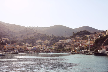 Colourful houses of the picturesque Symi island, holiday island of Dodecanese group close to Turkish coast north of Rhodes. Sunny summer evening. Dusk light. Greece. Landscape view from the water.  