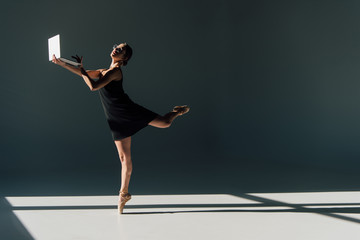 young ballerina in black dress and eyeglasses dancing with laptop