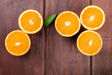 An overhead photo of fresh orange halves, shot from the top on a dark rustic wooden background with a green leaf and copy space