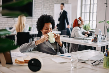 Happy African American businesswoman enjoying in her coffee time at work.