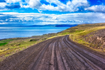 Fototapeta na wymiar Winding dirt road along the Atlantic coast of Iceland. Bright daytime landscape with amazing blue sky, the way to the Latrabjarg, the westernmost point in Iceland, outdoor travel background