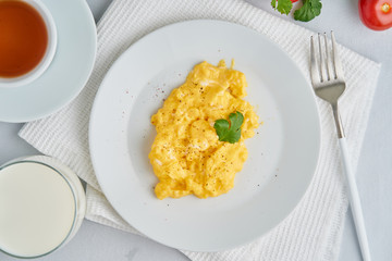 Breakfast with pan-fried scrambled eggs, cup of tea, tomatoes on white background. Omelette, top view