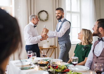 A man giving a bottle of wine to his father on indoor birthday party, a celebration concept.