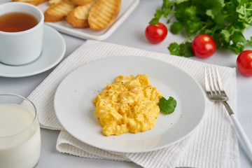 Scrambled eggs, omelet, side view. Breakfast with pan-fried eggs, glass of milk, tomatoes on white background.