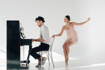 Fototapeta na wymiar handsome musician playing piano while beautiful ballerina dancing near chair