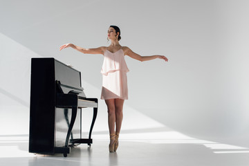 young attractive ballerina dancing near black piano