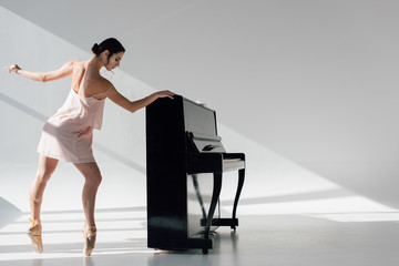 beautiful young ballerina dancing in sunlight near black piano