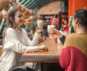 Two happy women are sitting in a cafe, drinking milkshakes,