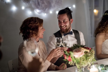 Young groom and his mother sitting at a table on a wedding, clinking glasses.