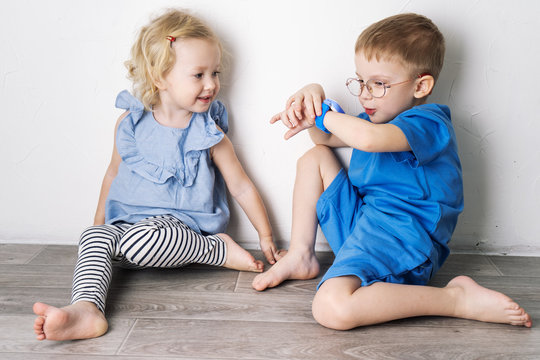A little boy child in a blue T-shirt and glasses shows the girl his smart watch and presses a finger.