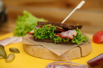 Grilled dark bread sandwich on wooden plate on yellow board