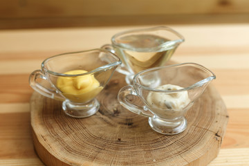 Set of three transparent sauceboats with different sauces on wooden plate