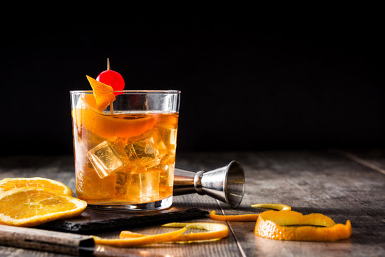 Old fashioned cocktail with orange and cherry on wooden table. Copyspace