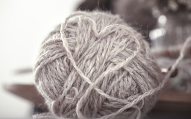Vintage wooden spokes and threads for knitting in the shape of a heart on a wooden plate. Still life photo