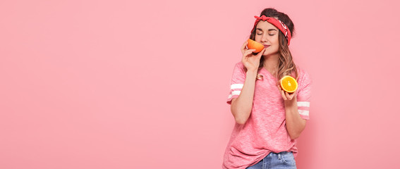 Beautiful young girl in pink t-shirt, keeps funny sexy orange on pink background. Summer and rest