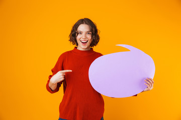 Image of joyous girl holding thought bubble with copyspace while standing isolated over yellow background