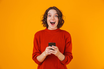 Fototapeta premium Portrait of caucasian woman holding and using cell phone while standing isolated over yellow background