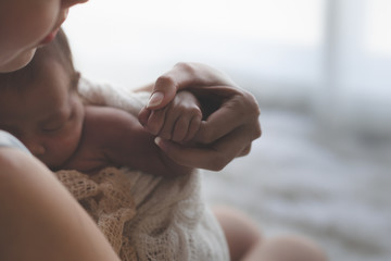 Close up Mother holding hands Asian female newborn baby  and sunlight in the morning. Cute little girl  three weeks old. Health, care, love, relationship concept. - obrazy, fototapety, plakaty