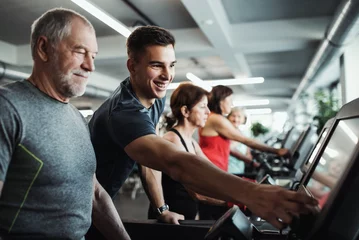 Foto auf Acrylglas Fitness Eine Gruppe von Senioren im Fitnessstudio mit einem jungen Trainer, der Cardio-Training macht.