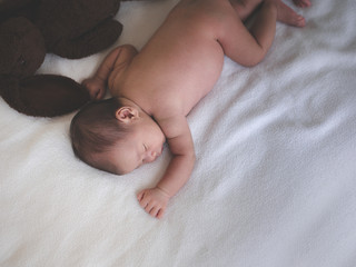 Asian female newborn baby sleeping in bed with dolls and sunlight in the morning. Cute little girl three weeks old. with copy space