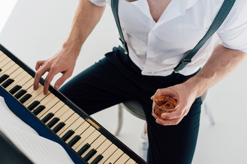 cropped view of pianist holding glass of alcohol drink while playing piano