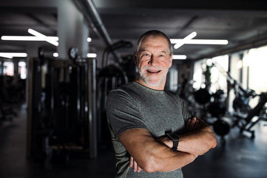 A cheerful senior man standing in gym, arms crossed.