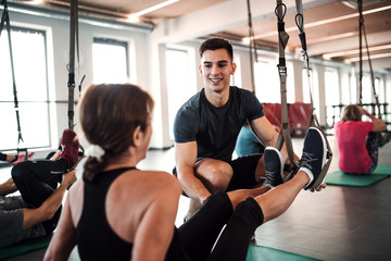 A group of cheerful seniors in gym with a young trainer doing exercise with TRX.